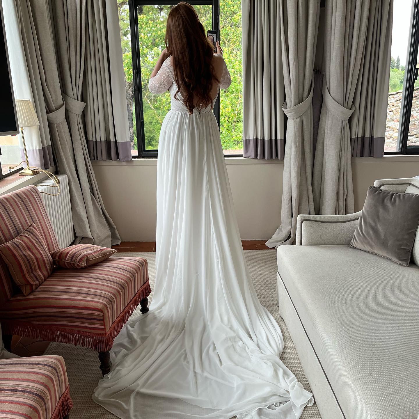 Bride talking on the phone while looking out the window where she had her hair and makeup done by Adrienne Aereboe.